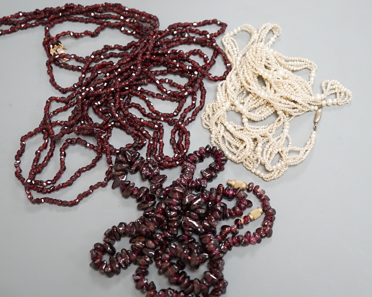 An early 20th century triple strand facet cut garnet necklace, with yellow metal clasp, 122cm, a similar single strand garnet 'pebble' necklace and a seed pearl necklace, 118cm.